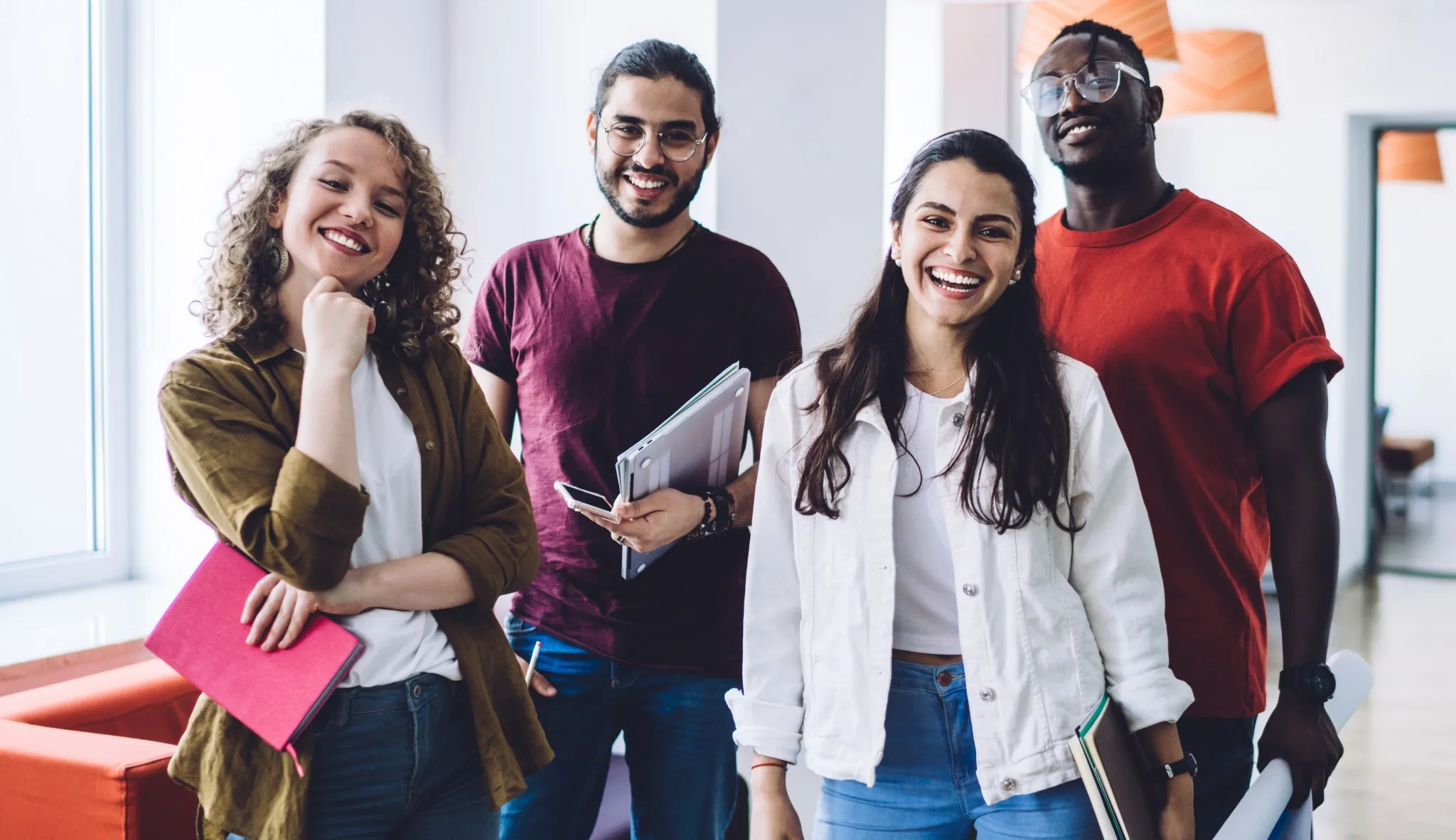 Uma equipe de estudantes de diferentes etnias, com cadernos nas mãos e sorrindo para foto.
