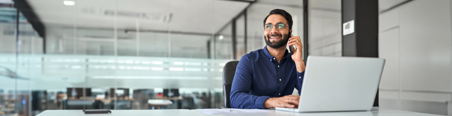 Um homem trabalhando no escritório, sorrindo e falando no celular.