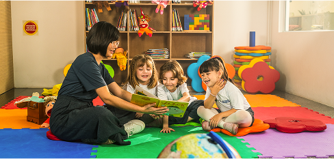 Professora com três crianças lendo um livro enquanto se divertem