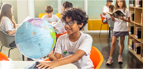 Menino em sala de aula olhando para um globo terrestre giratório