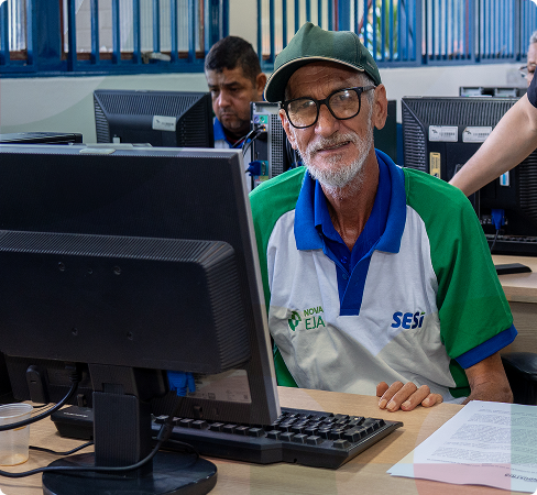 Senhor sorri para a câmera enquanto utiliza o computador em uma sala de aula.